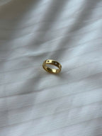A gold band ring with a textured, beaded outer edge and a smooth inner band, resting on a white textured fabric surface.