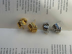 Two spiral hoop earrings, one silver-toned and one gold-toned, displayed on an open book page with recipe text visible.
