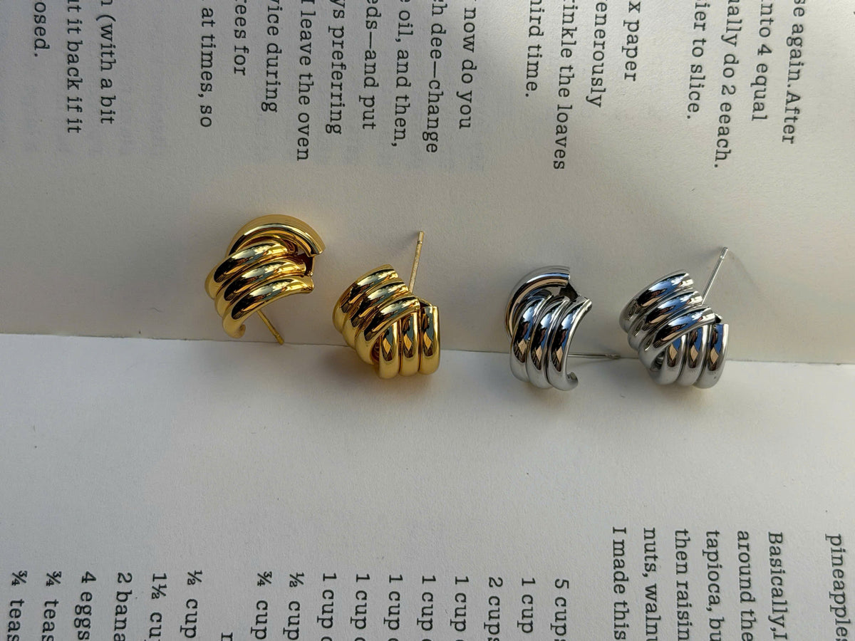 Two spiral hoop earrings, one silver-toned and one gold-toned, displayed on an open book page with recipe text visible.