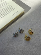 Three small spiral hoop earrings in silver and gold tones arranged on a textured light gray surface next to an open book.