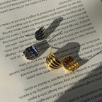 Two small metallic hoop earrings, one silver and one gold, displayed on an open book page with text visible in the background.