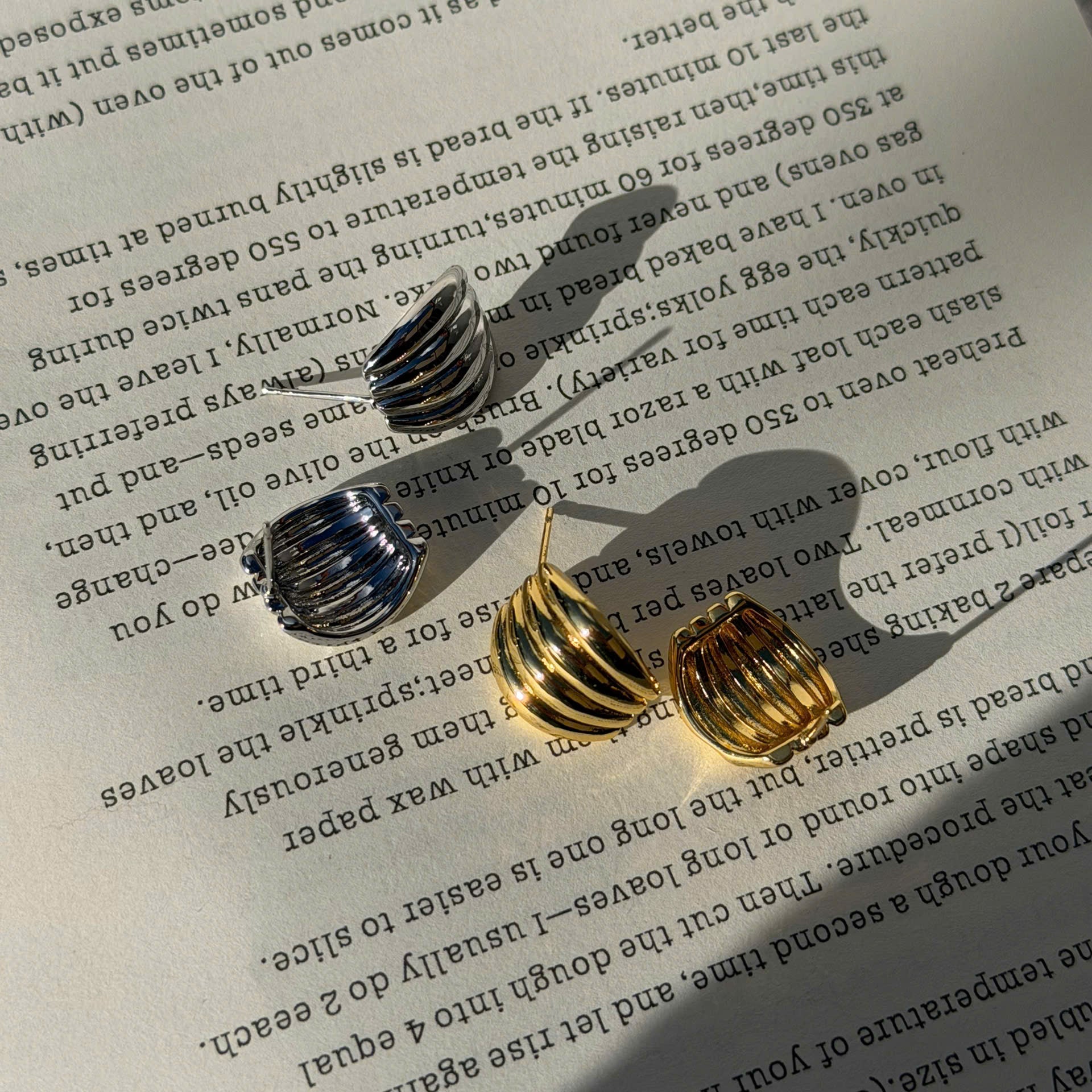Two small metallic hoop earrings, one silver and one gold, displayed on an open book page with text visible in the background.