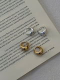 Three small hoop-style earrings in silver and gold tones arranged on an open book page.