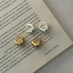 Four small hoop earrings in gold and silver tones arranged on an open book page, with a textured light gray surface visible around the book.