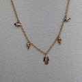 A delicate gold chain necklace featuring small dangling charms, including a central hamsa hand pendant and smaller bird-like accents, displayed on a textured off-white background.