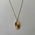 A gold chain necklace with a textured, sunburst-style oval pendant, displayed against a plain light gray background.