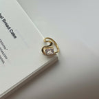 A gold-plated ring with a clear rectangular gemstone, resting on the edge of a white book against a light gray background.