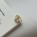 A gold-plated ring with a rectangular clear gemstone, resting on the edge of a white book against a light gray background.