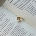A gold ring with a clear rectangular gemstone resting on an open book with printed text.