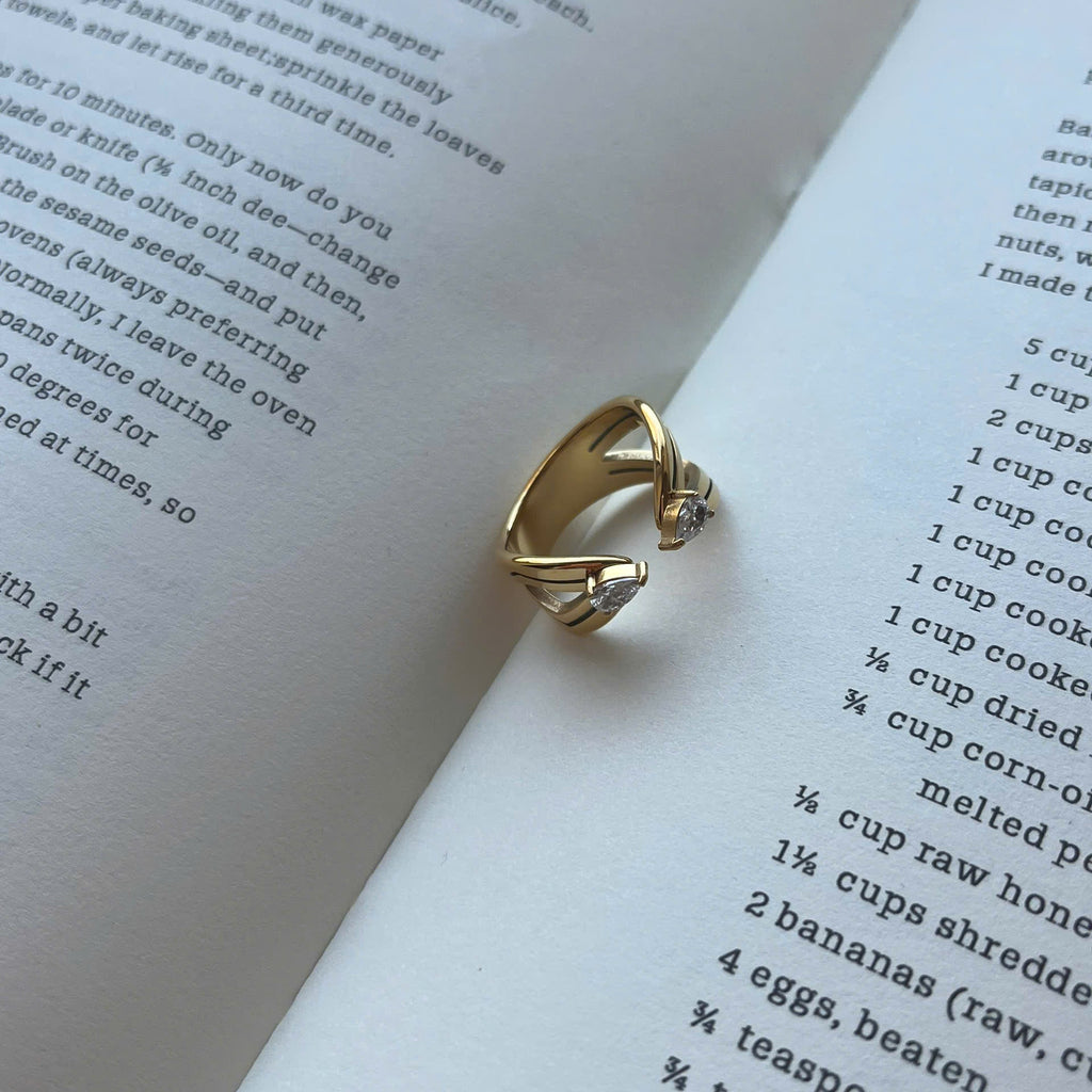A gold ring with a small clear gemstone, styled on the pages of an open book.