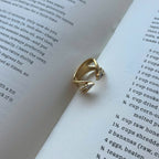 A gold ring with a small clear gemstone, styled on the pages of an open book.