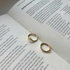 Two small gold hoop earrings resting on the pages of an open book with printed text.