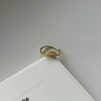 A delicate gold ring with a small sunburst or fan-like motif on the front, resting on the corner of a white book against a light gray background.