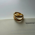 A gold-toned twisted ring with three interlocking bands, resting on the edge of an open book against a light gray background.