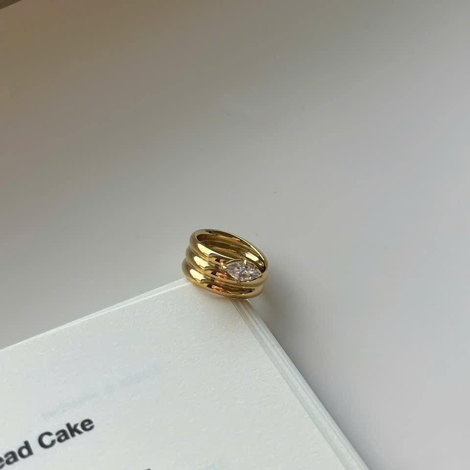 A gold ring with a clear round gemstone, resting on the edge of an open book against a light gray background.