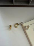 Four twisted metal hoop earrings in gold and silver finishes arranged on a light surface next to an open book.