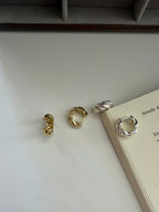 Four twisted metal hoop earrings in gold and silver finishes arranged on a light surface next to an open book.