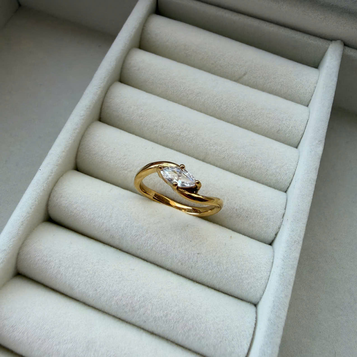 A gold ring with a marquise-cut clear gemstone displayed on a white velvet ring box.